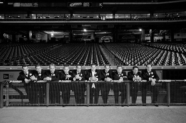 black and white photo - groom and groomsmen in tuxedos leaning on gate at an empty sports stadium - photo by Houston based wedding photographer Adam Nyholt